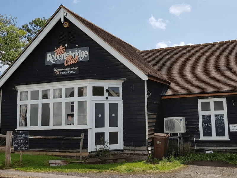 The Robertsbridge Club clubhouse: a black weatherboarded building with white window frames, the club's own sign above the entrance, and a tiled roof